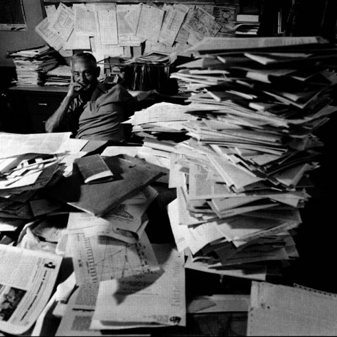 Bill Hanson sitting at a desk stacked high with papers